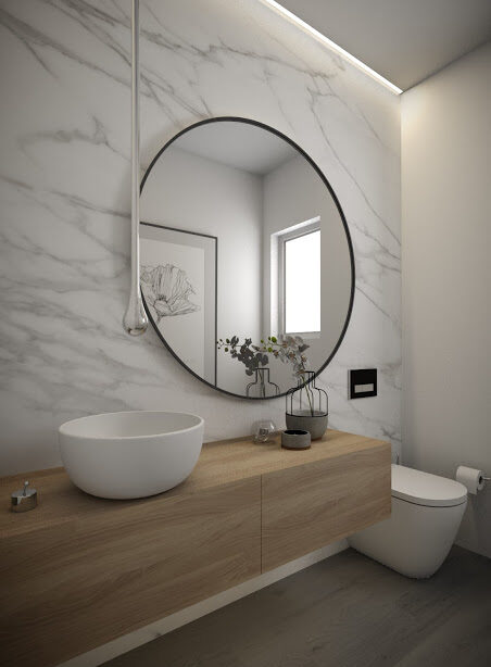 A contemporary bathroom featuring sleek white marble walls, adorned with a circular mirror and wood vanity.