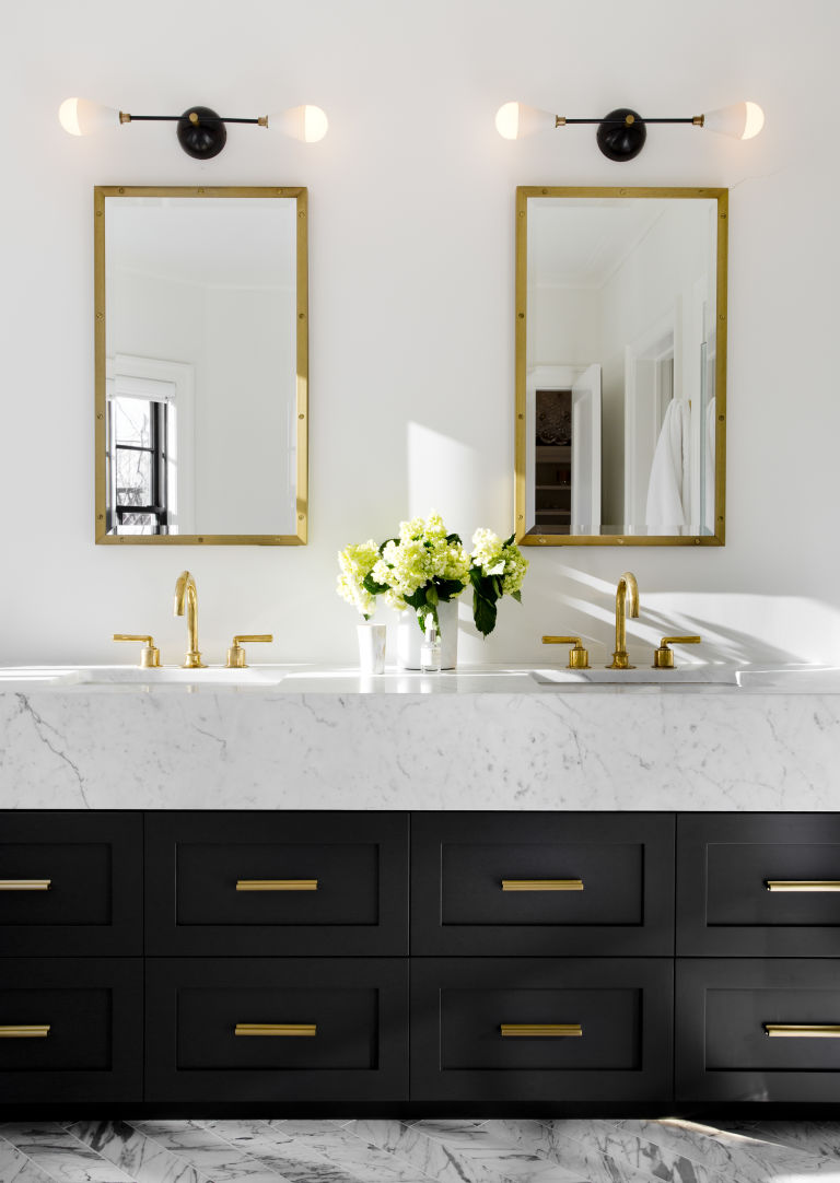 White bathroom with black drawers, finished with gold fixtures.