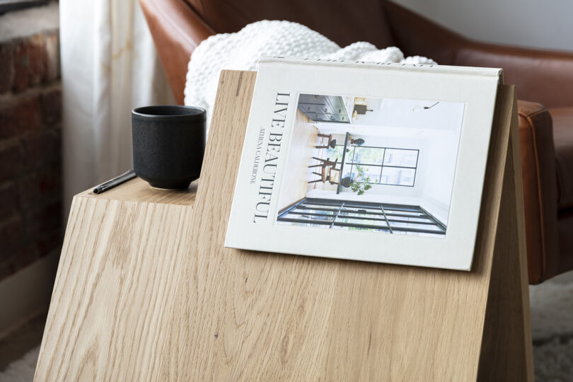 detail of triangle-shaped wooden side table holding a book and mug