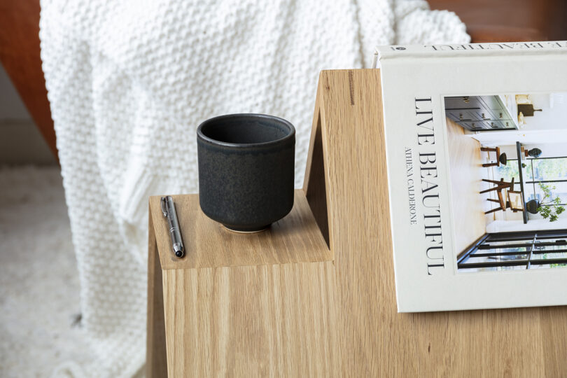detail of triangle-shaped wooden side table holding a book and mug