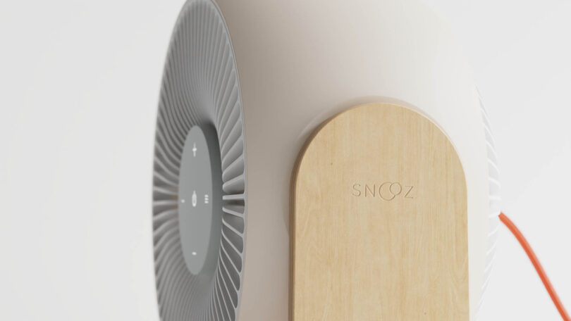 Detail side of the Snooz Breez fan focused upon the bent plywood stand's left side imprinted with a subtle Snooz logo; the fan's red cord can be seen snaking out from the right side.