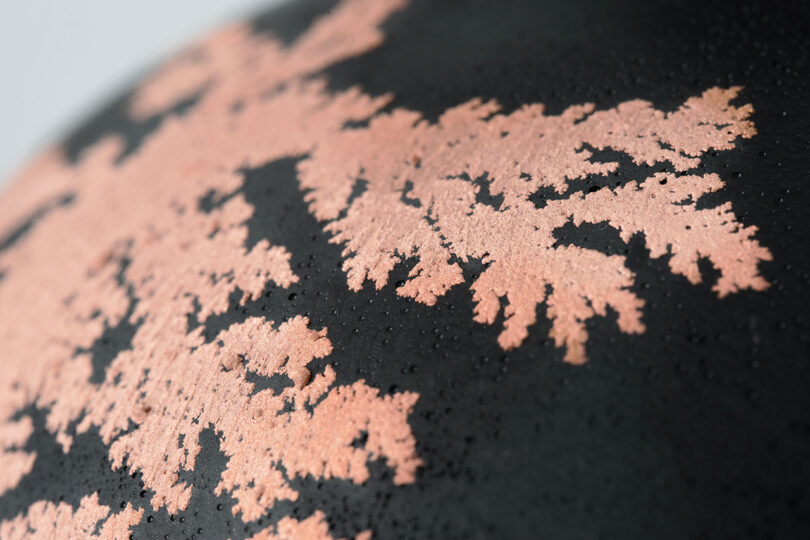 detail of black orb covered in spots of copper moss