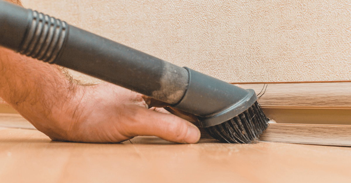 Closeup of vacuum with brush attachment cleaning baseboards.