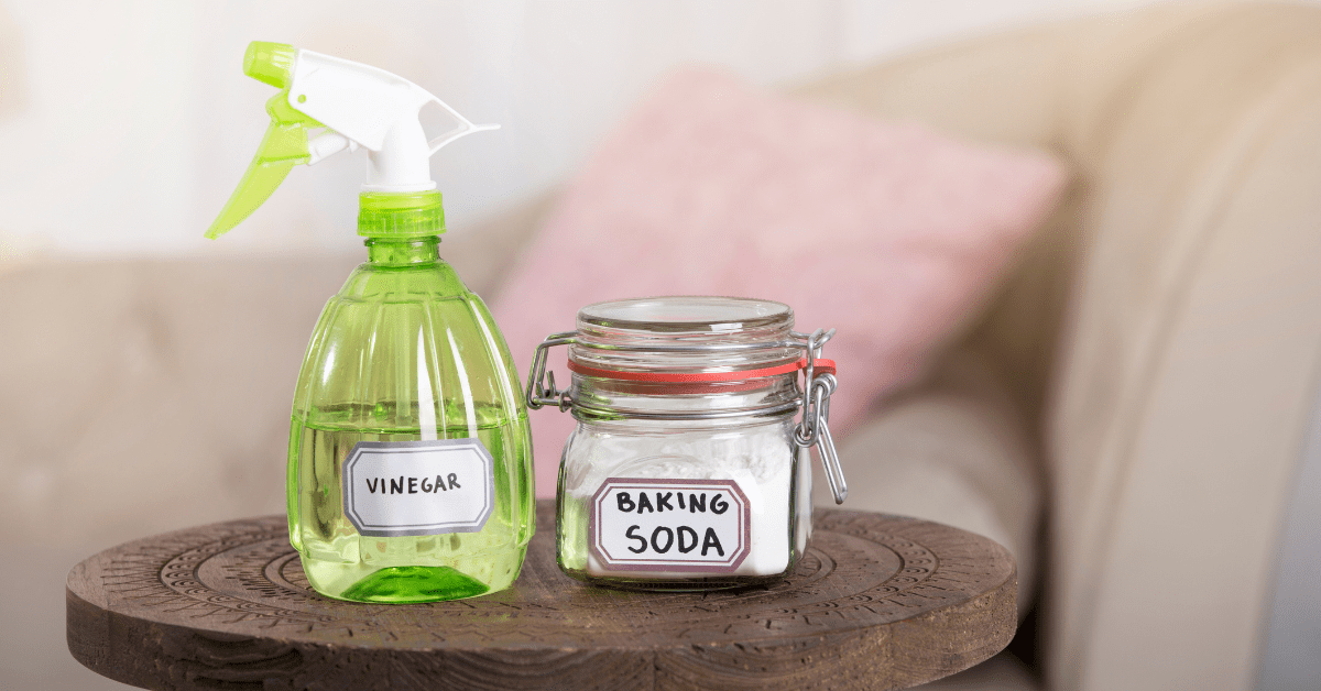 A spray bottle of vinegar and glass container of baking soda placed on a table.