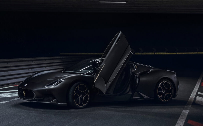 Side view of Maserati MC20 Notte Edition super sports car in matte and glossy black finish with gull wing driver's door opened.