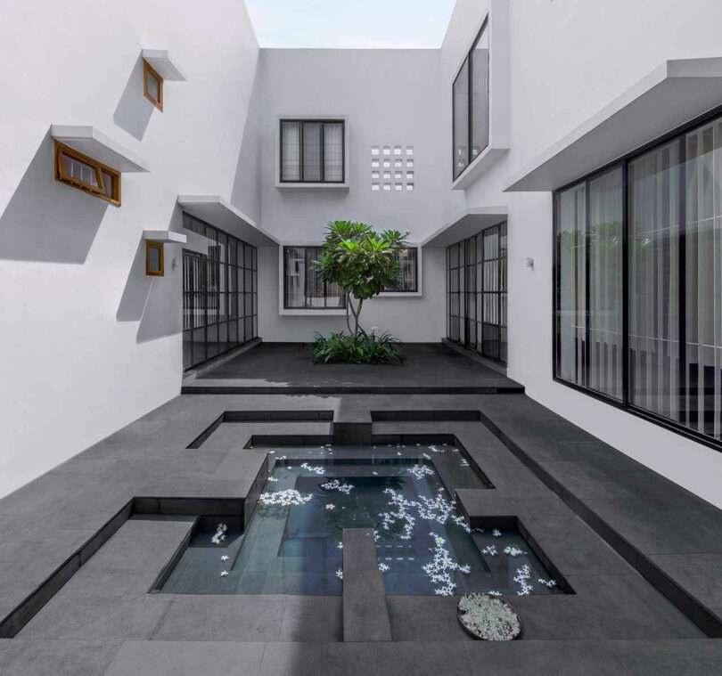Exterior shot of wrap around white house with geometric black floored courtyard with geometric water feature