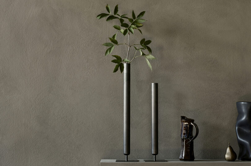 two dark, slim vases on a styled surface