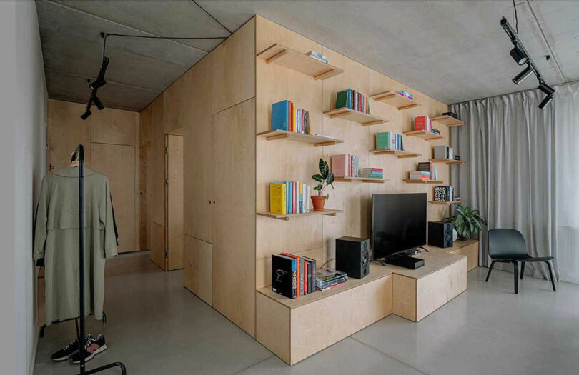 angled view of light wood box structure within an apartment holding shelves of books and TV