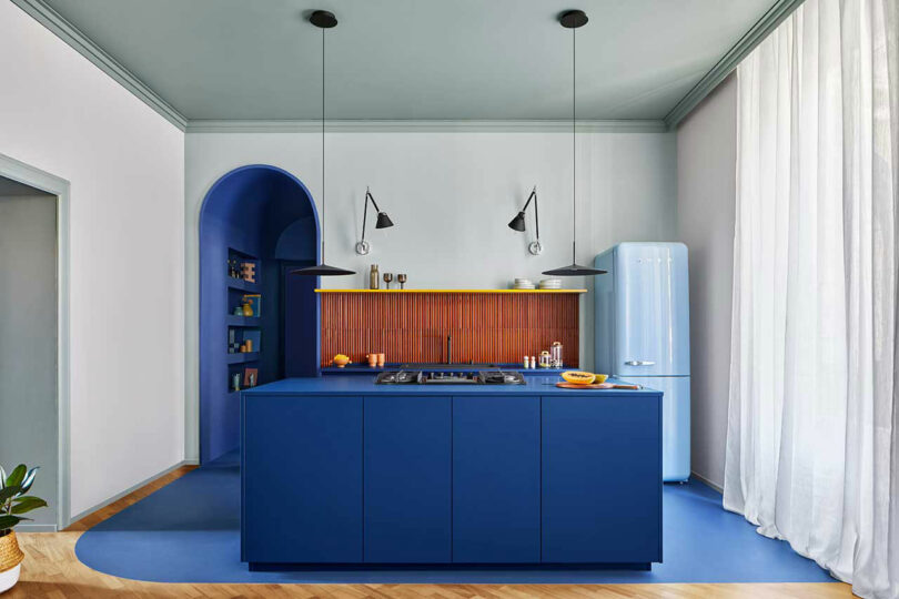 Modern kitchen interior with vibrant blue island and dark red tiles