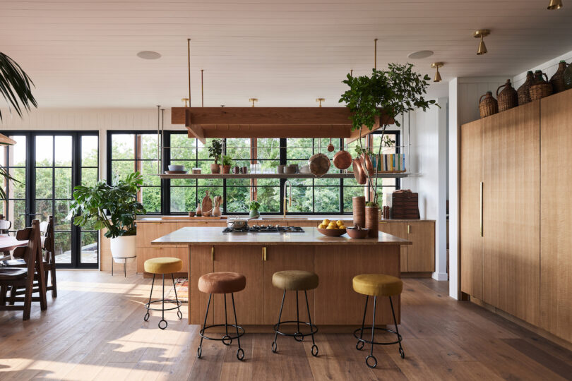 Large open air residential kitchen with four metal wire feet stool chairs surrounding a kitchen island with floating shelf above.