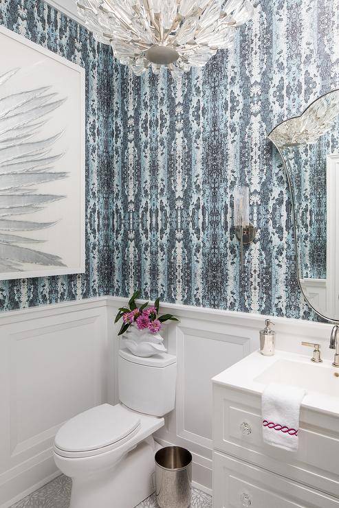 Sophisticated white and blue powder room features blue wallpaper over white wainscoting.