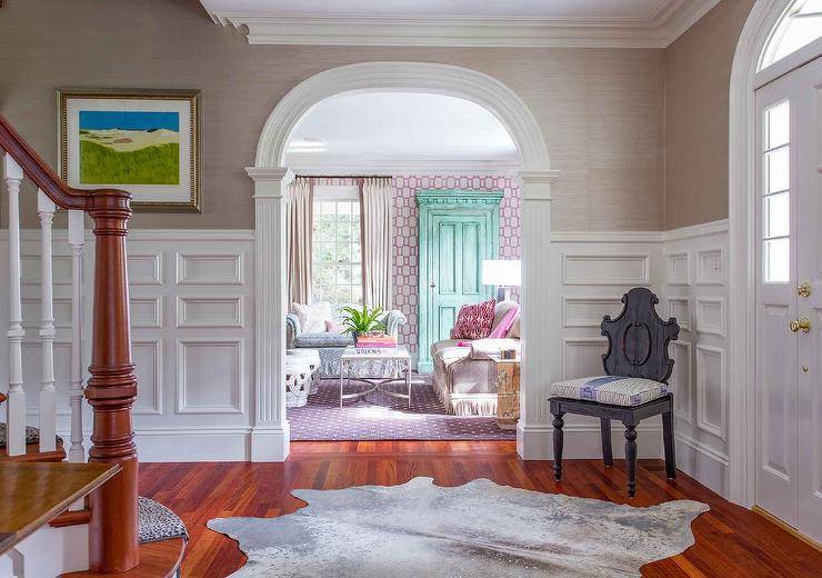 Foyer boasting stacked wainscoting and gray grasscloth wallpaper finished with a vintage gray chair and a cowhide accent rug on oak wood floors.