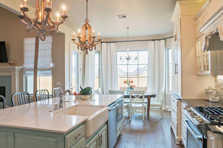 Beautiful and functional kitchen with farmhouse flair and traditional elements of design. White cabinets are perfectly paired with a glass tile backsplash, and the green kitchen island gives the room a fresh, modern feel. A farmhouse sink and statement lighting, along with abundant natural light, help make the space functional, as well as inviting.