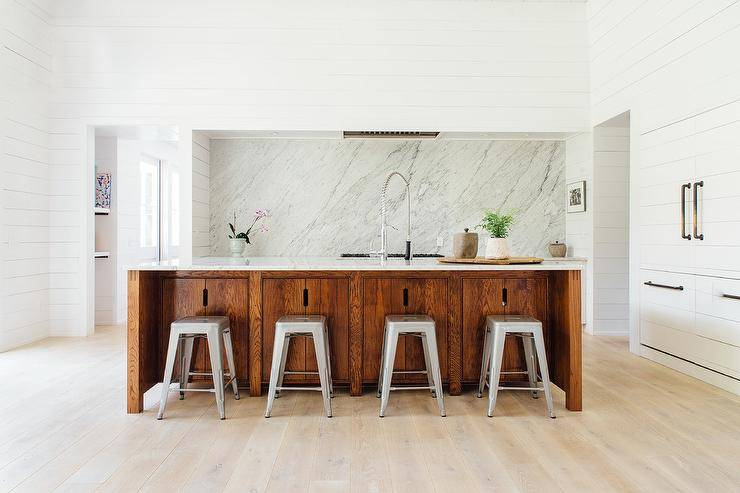 Large open concept kitchen design completed with shiplap walls merging into appliances concealed with white shiplap and accented with oil rubbed bronze hardware! This allows a clean, simple and minimalistic space to showcase with a cottage feel. The large center island is a stained oak finish with white marble countertops paired with Tolix stools.