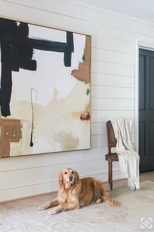 Large abstract art with beige and black tones displayed on shiplap wall. Brown carpet adds to the warm tones complimenting the oversized wall art canvas.