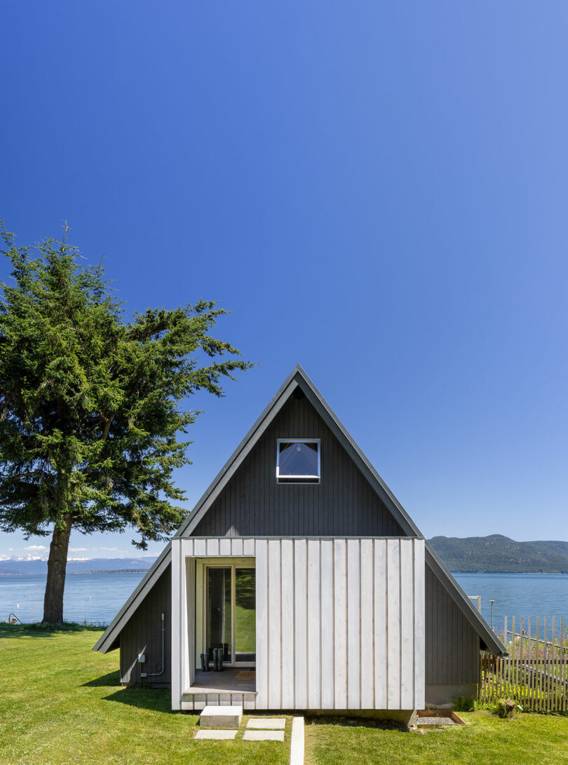 back exterior view of modern gray a-frame cabin with water behind