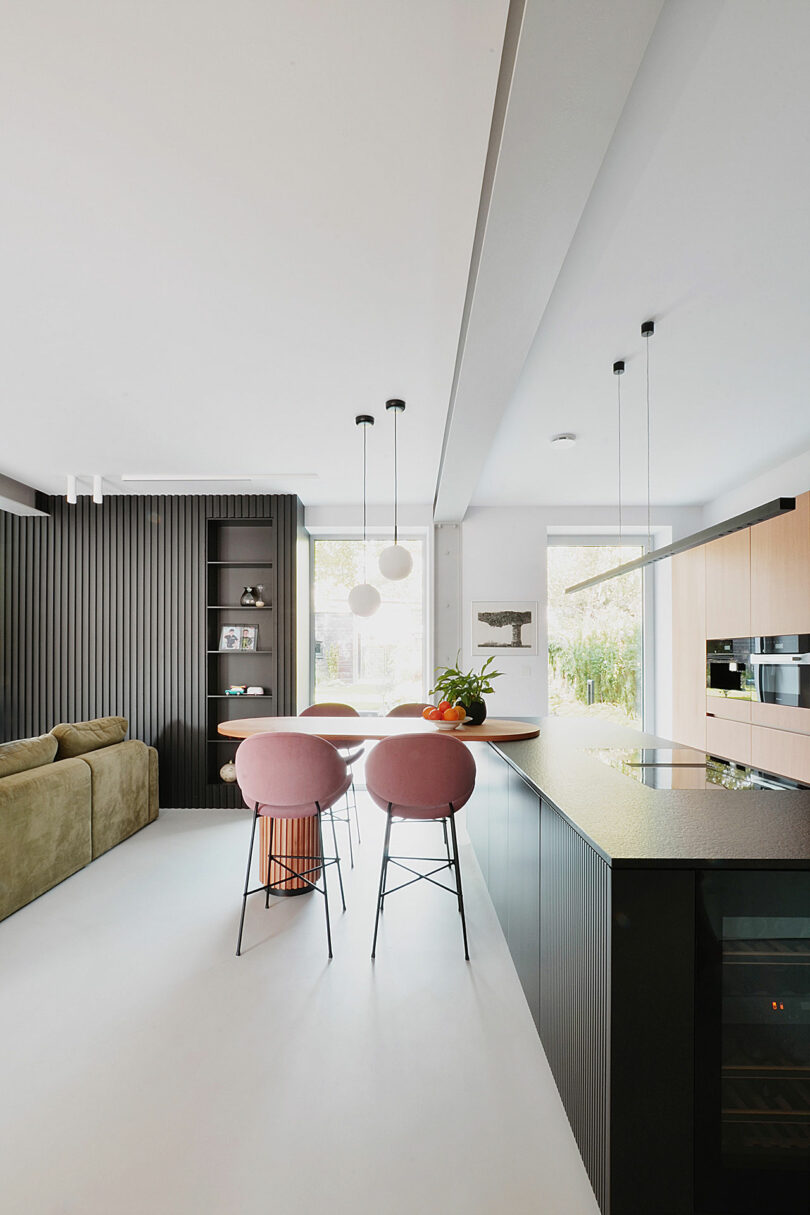 side interior view into modern kitchen with wood cabinets, black island, and wood bar table with pink stools