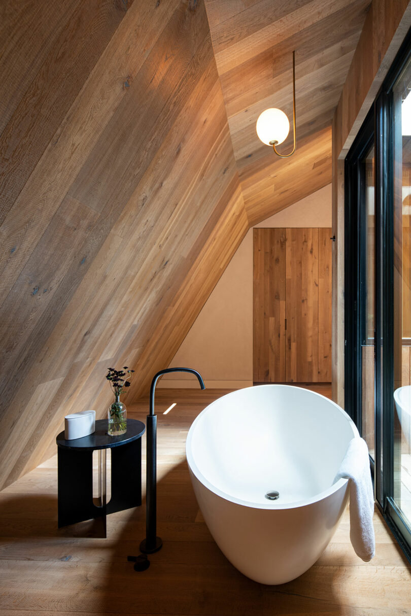 modern bathroom with floating white tub under sloped wood ceiling