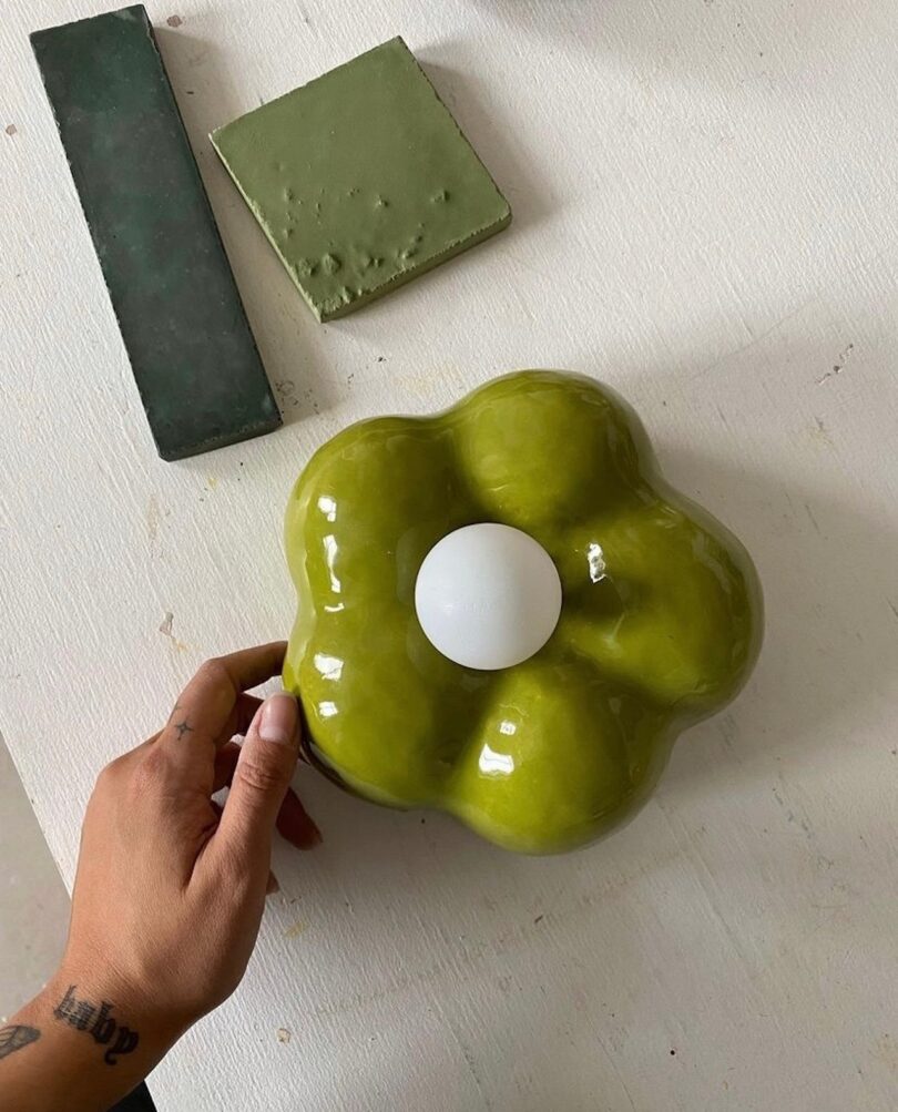 hand touching a ceramic green flower next to tile samples