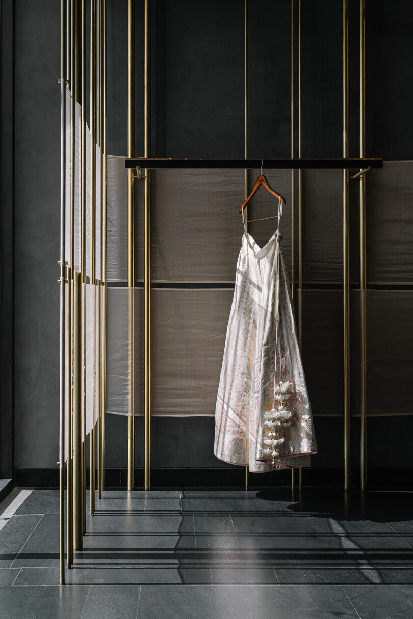 Vertical gold rods from which shelves are built and garments hang. White dress hangs.
