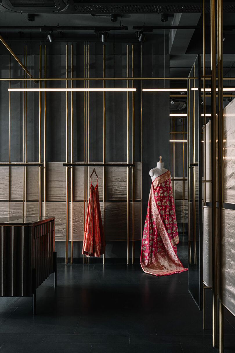 Vertical gold rods from which shelves are built and garments hang. Two dresses displayed.