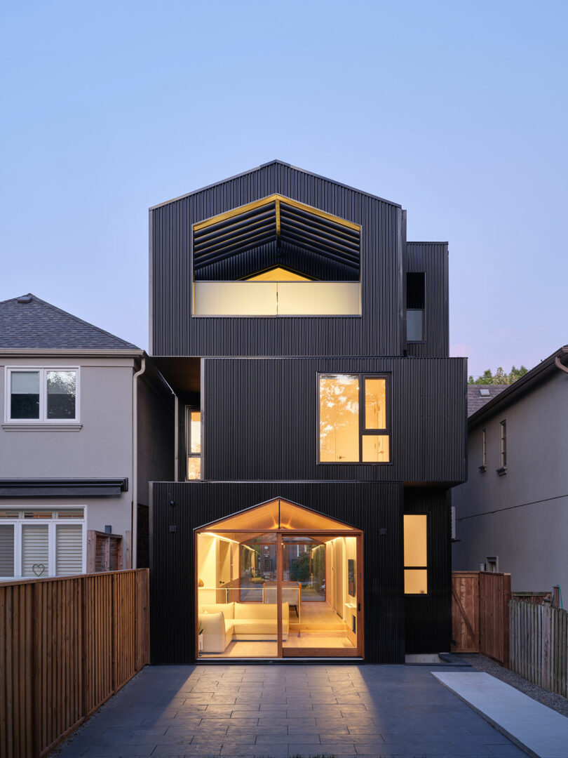 rear exterior evening view of modern three story stacked house in evening with yellow lighting shining through windows