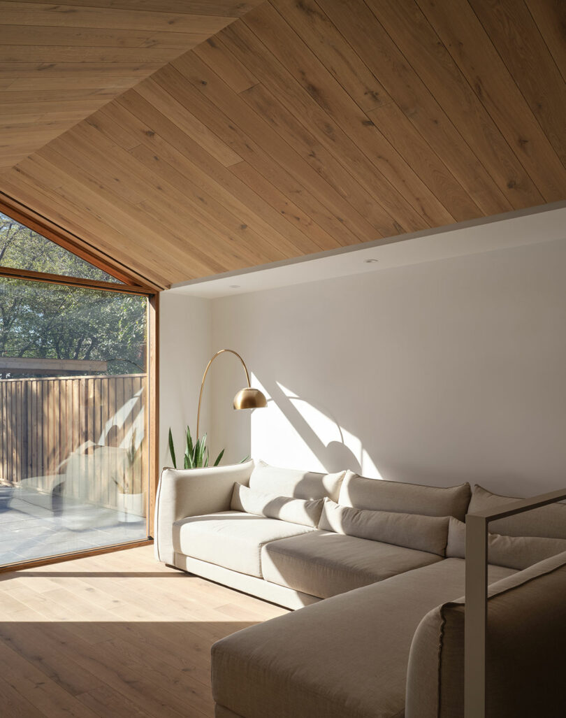 angled interior view of modern minimalist living room with modular white sofa with wood gable ceiling