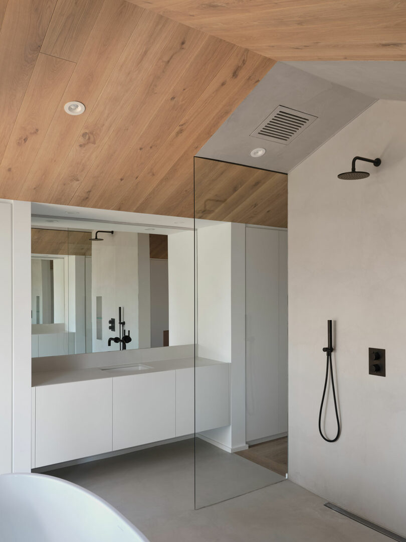 angled view of modern minimalist bathroom with all white walls and cabinetry and light wood gabled ceiling