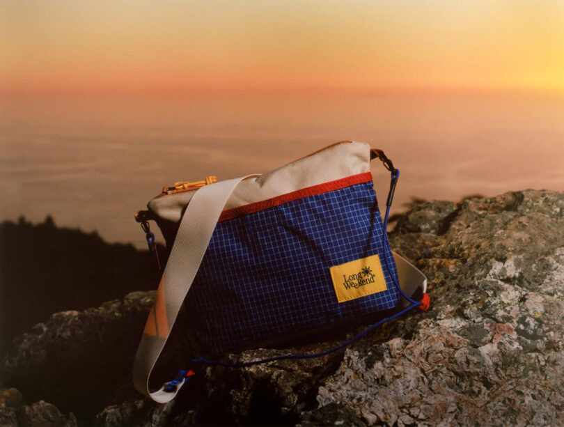 Long Weekend Camera Line bag set on ragged mountainside rock overlooking a clouded and sunset tinged landscape below.