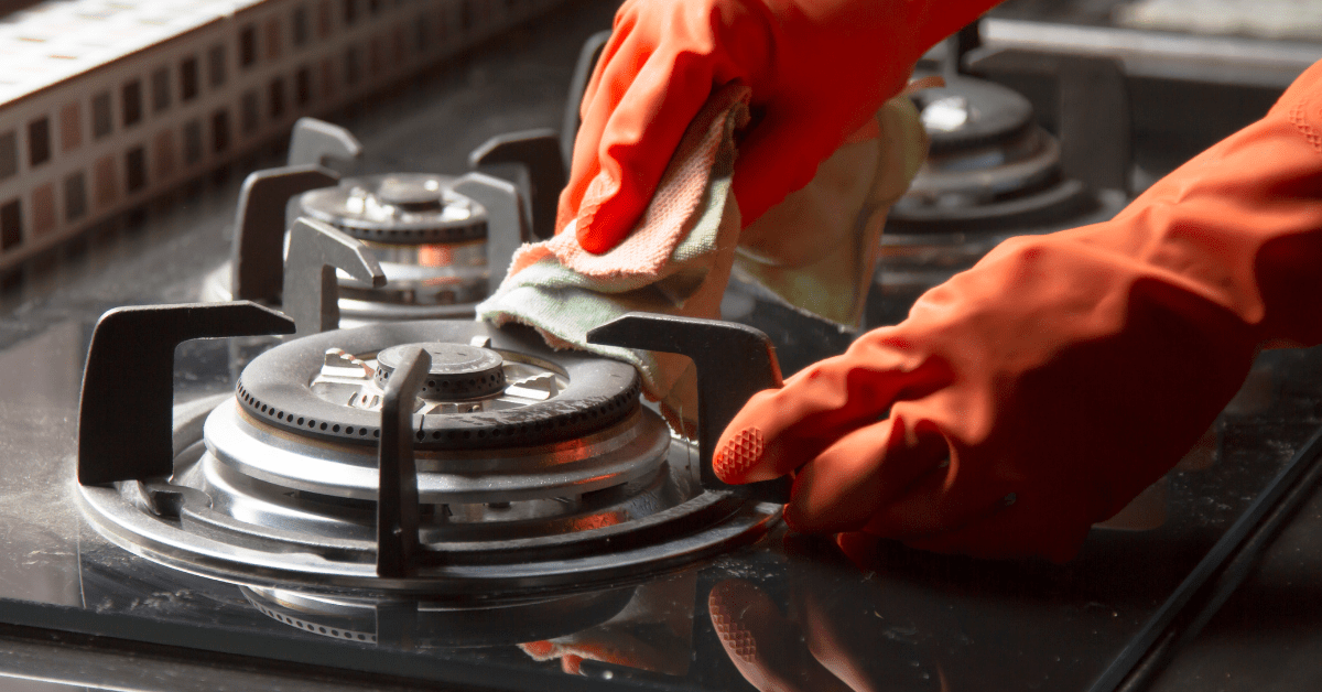 A person wearing orange gloves scrubbing down stove grates.