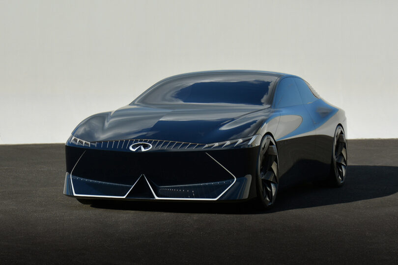 All-electric Vision Qe fastback sedan parked on black asphalt with white wall in the background.