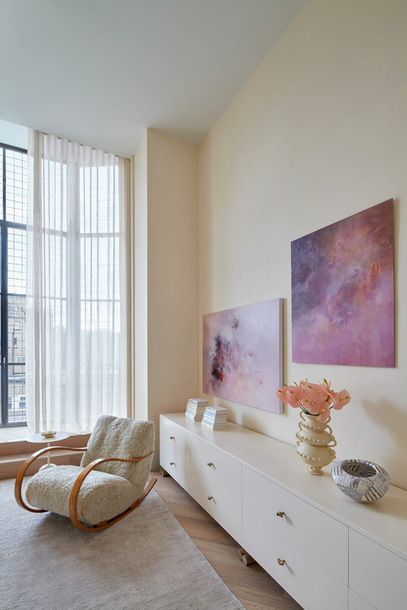 angled interior view of modern bedroom on side with lounge chair and low white console with two purple pink paintings above