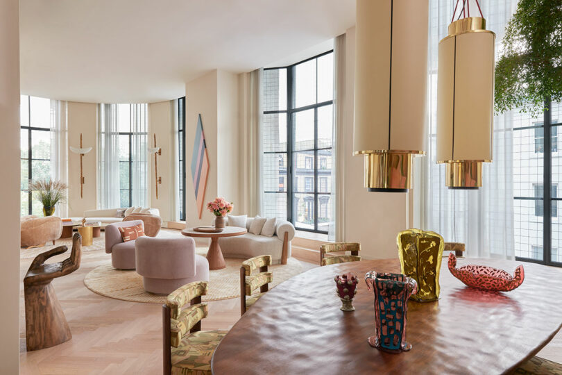 view over unique dining table looking into open modern living space with pastel upholstered chairs in living room and seating area