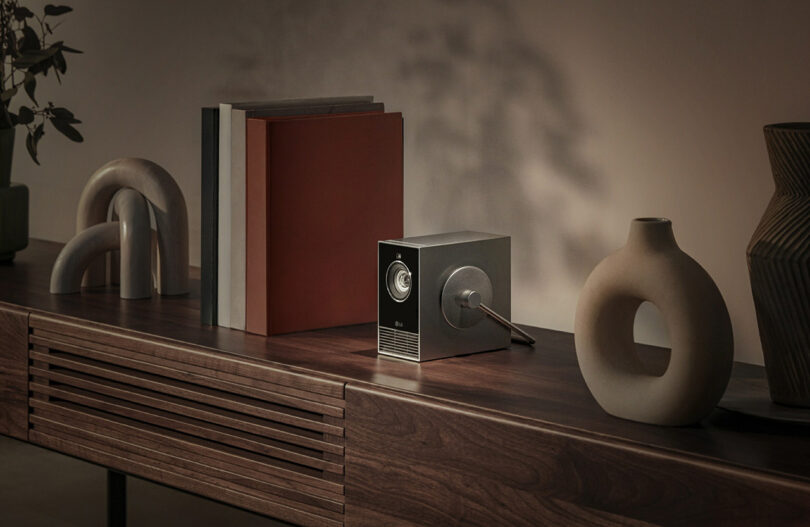 LG CineBeam Qube projector on a wood console set next to books and ceramics, showcasing its small size.