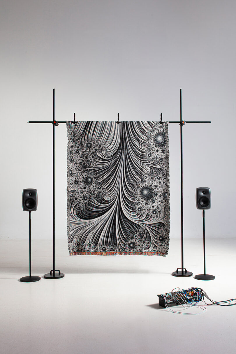 black and white patterned textile hanging on a rack with two speakers nearby