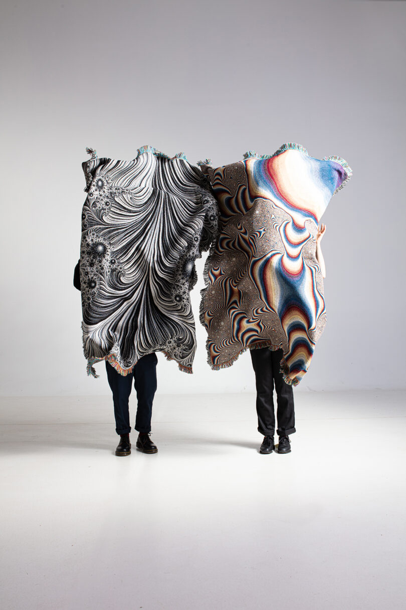 two people standing side by side holding up patterned textiles