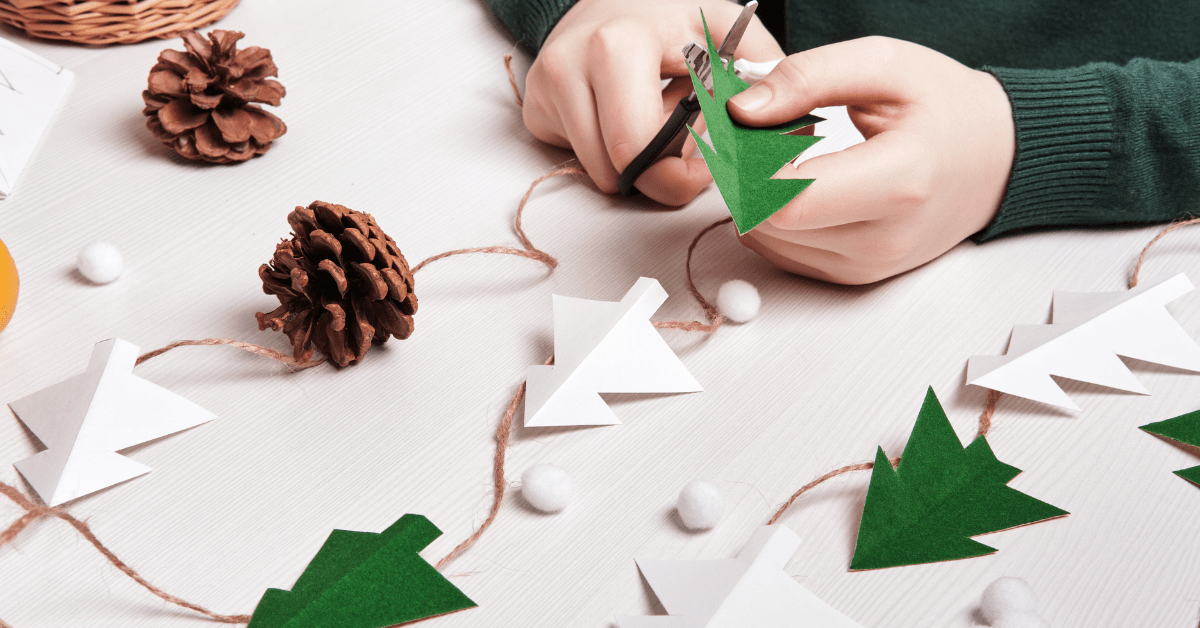 Closeup of someone's hand cutting Christmas trees with pine cones nearby.