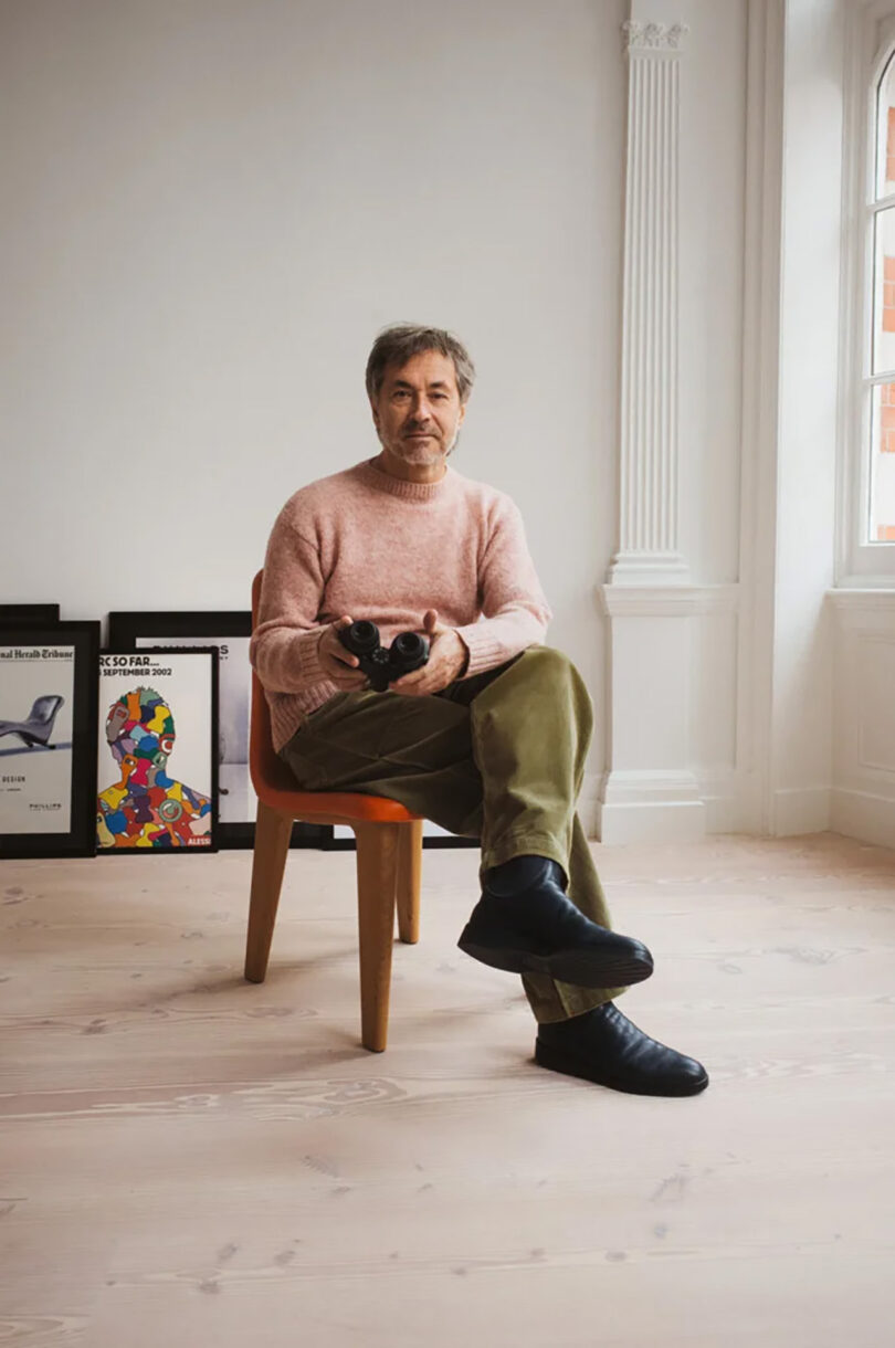 Designer Marc Newson seated holding a pair of SWAROVSKI OPTIK AX Visio smart binoculars with his legs crossed.