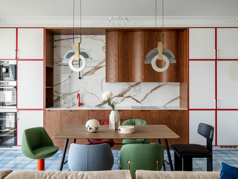 front facing interior view of modern kitchen with wavy wood cabinets, dining table, and a mix of colorful dining chairs