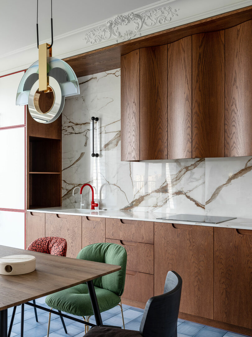 angled close up interior view of modern kitchen with wavy wood cabinets, dining table, and a mix of colorful dining chairs