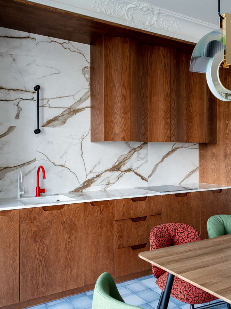 closeup partial interior view of modern kitchen with wavy wood cabinets, dining table, and a mix of colorful dining chairs