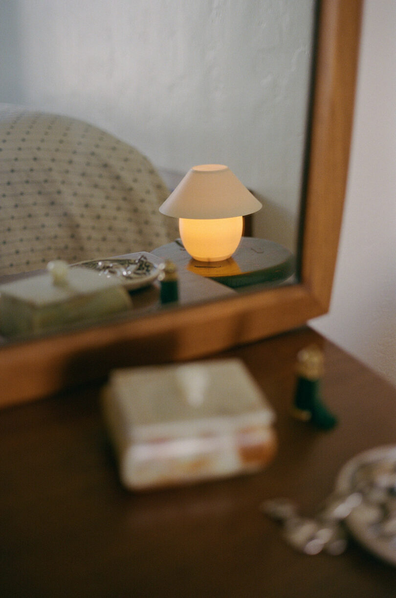 A tiny orb-shaped lamp with traditional shade sitting on a stool in the reflection of a mirror.