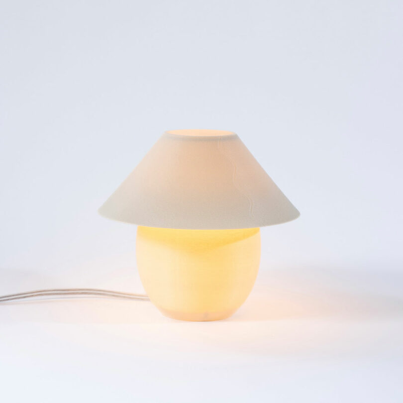 A tiny, eggshell colored orb-shaped lamp with traditional shade turned on.