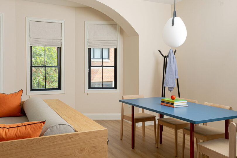 YOWIE hotel living space with sofa and long dining table with four dining chairs, pendant lamp overhead, wood floors underneath and two pane windows at the far wall.