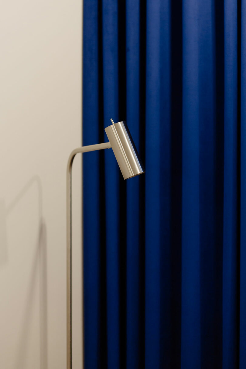 closeup of chrome lamp in front of gathered bright blue curtain