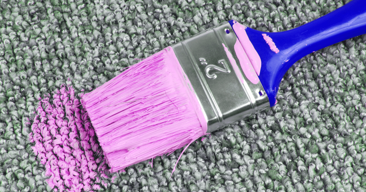Paint brush with pink paint on carpet.