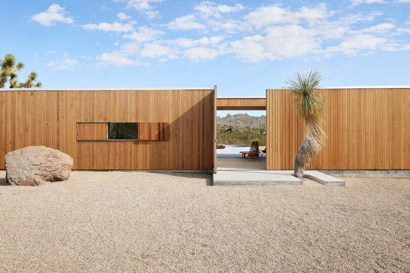 exterior view of modern wood pavilion style house in desert with large doors opening to covered patio