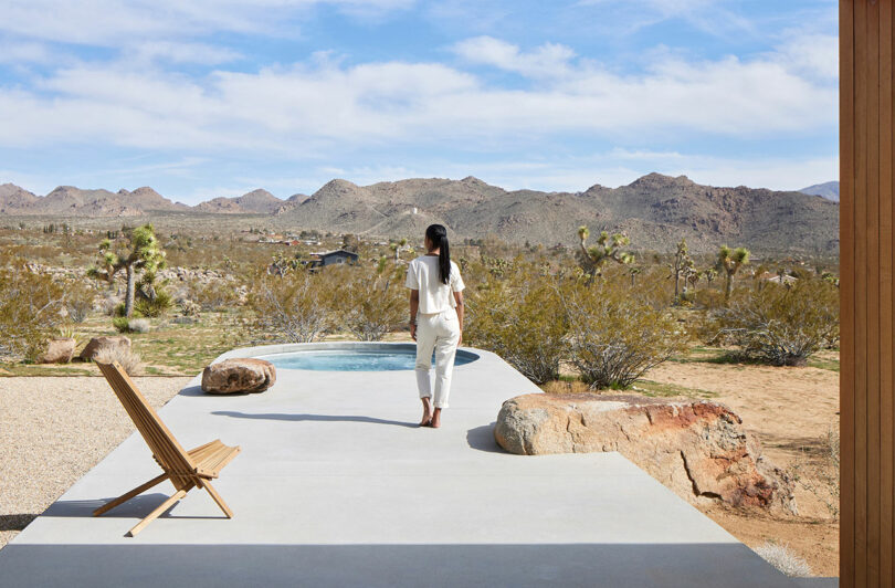 exterior view in desert of concrete patio leading to circular pool with woman walking away