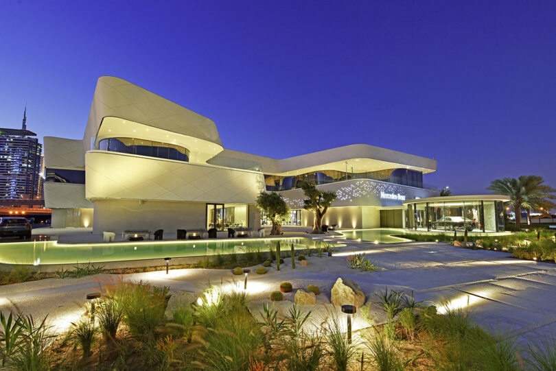 Early evening exterior shot of the Mercedes-Benz Brand Center in Dubai with landscaping lighting illuminating the walkways.