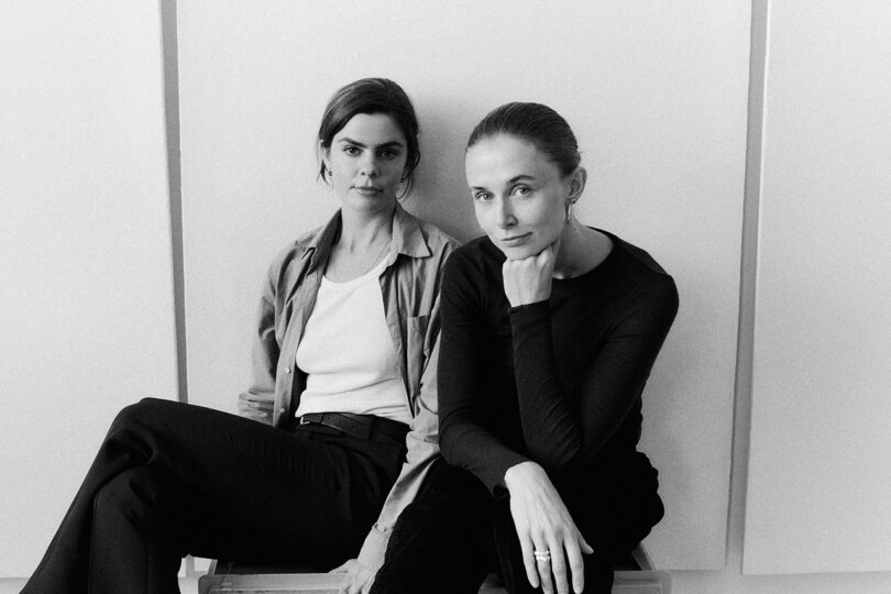 black and white image of two women sitting next to each other looking into the camera